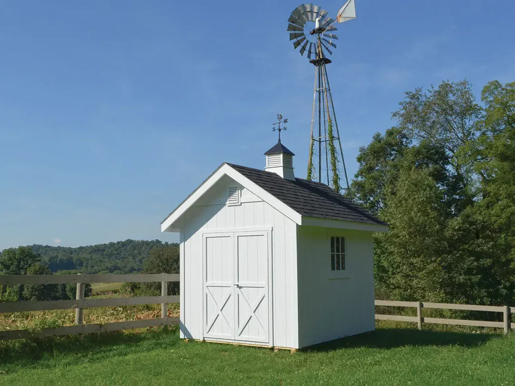 White utility storage shed with double barn doors and a cupola in an open field